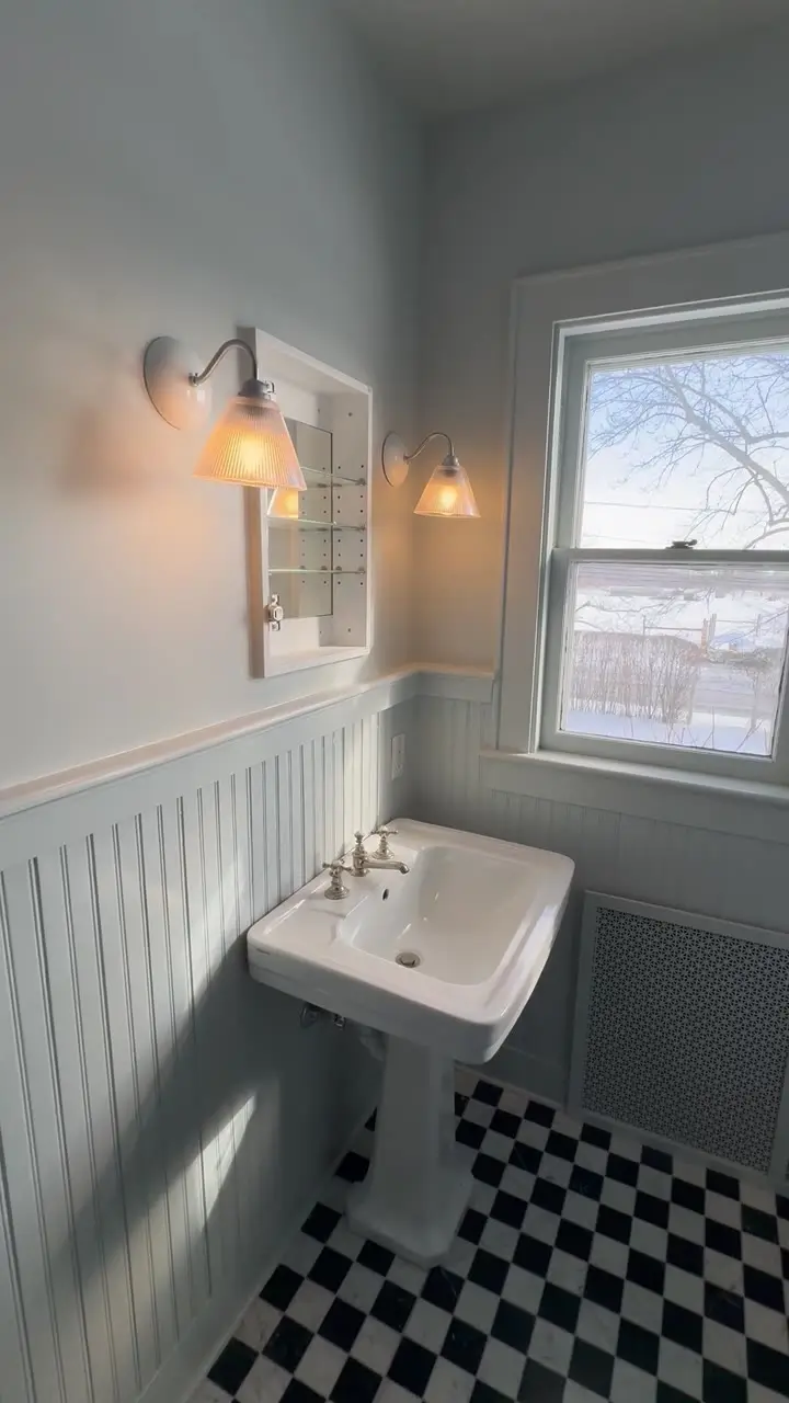 Powder room with pale blue-grey walls, white beadboard wainscoting and a checkerboard tile floor