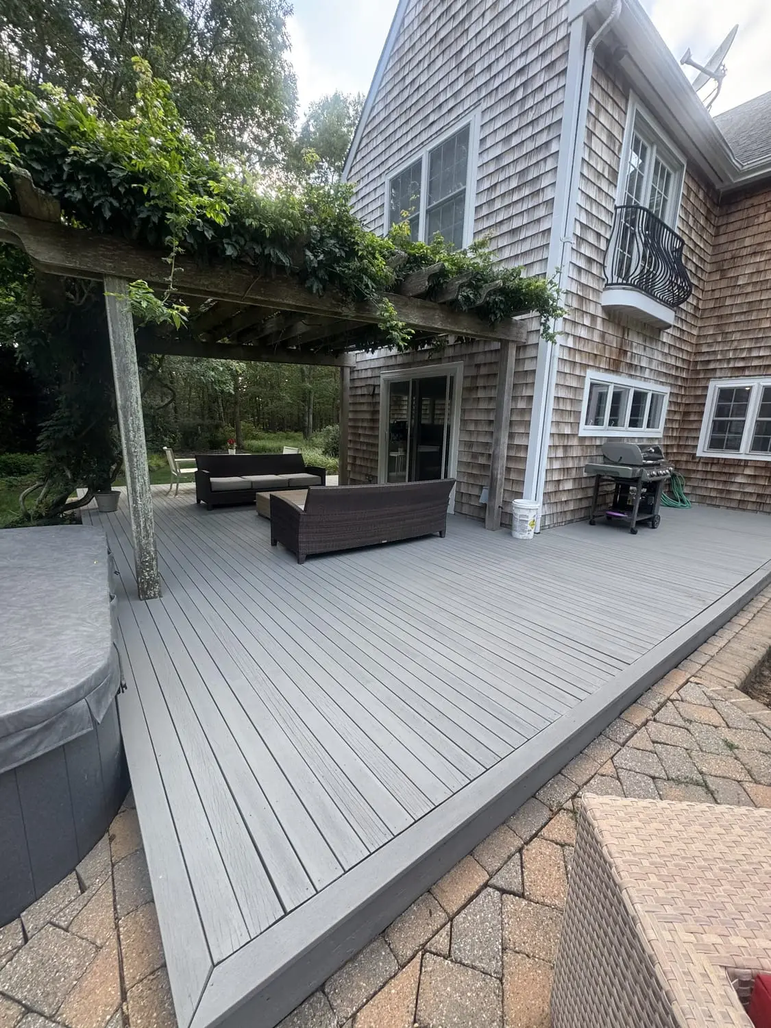 Refinished composite deck with pergola and paver patio behind a shingled home