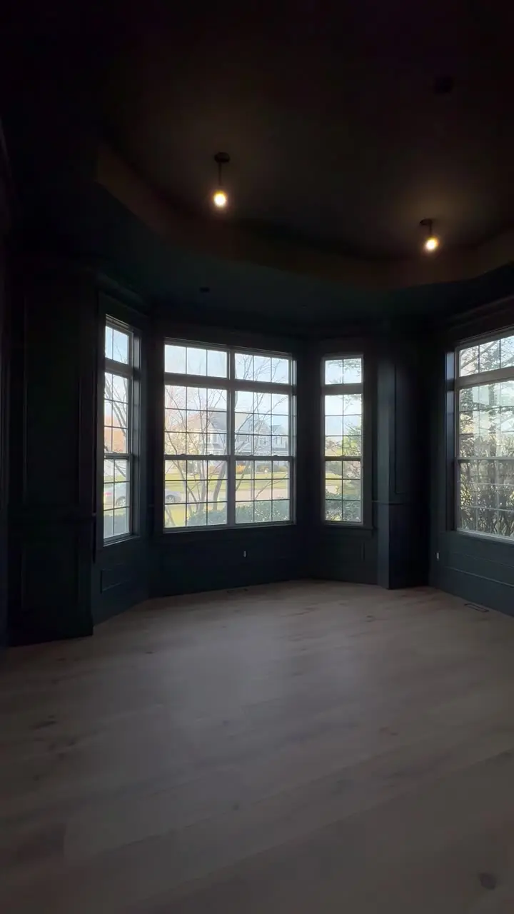 Room painted in deep navy with panelled walls and a bay window, warm light and pale wood floors
