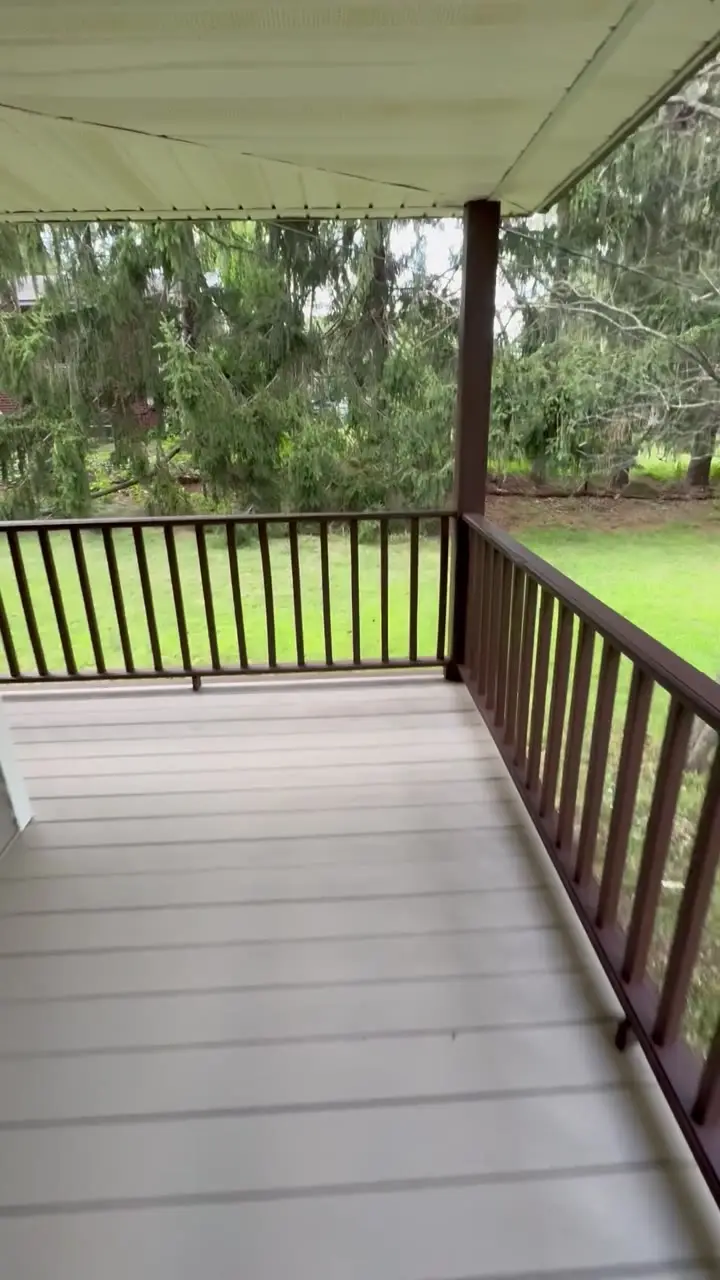 Covered front porch with a freshly painted grey deck floor and dark stained railings, overlooking a green lawn