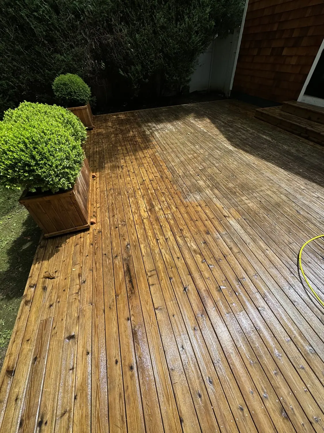 Wooden deck being soft washed clean beside a cedar-shingled Long Island home