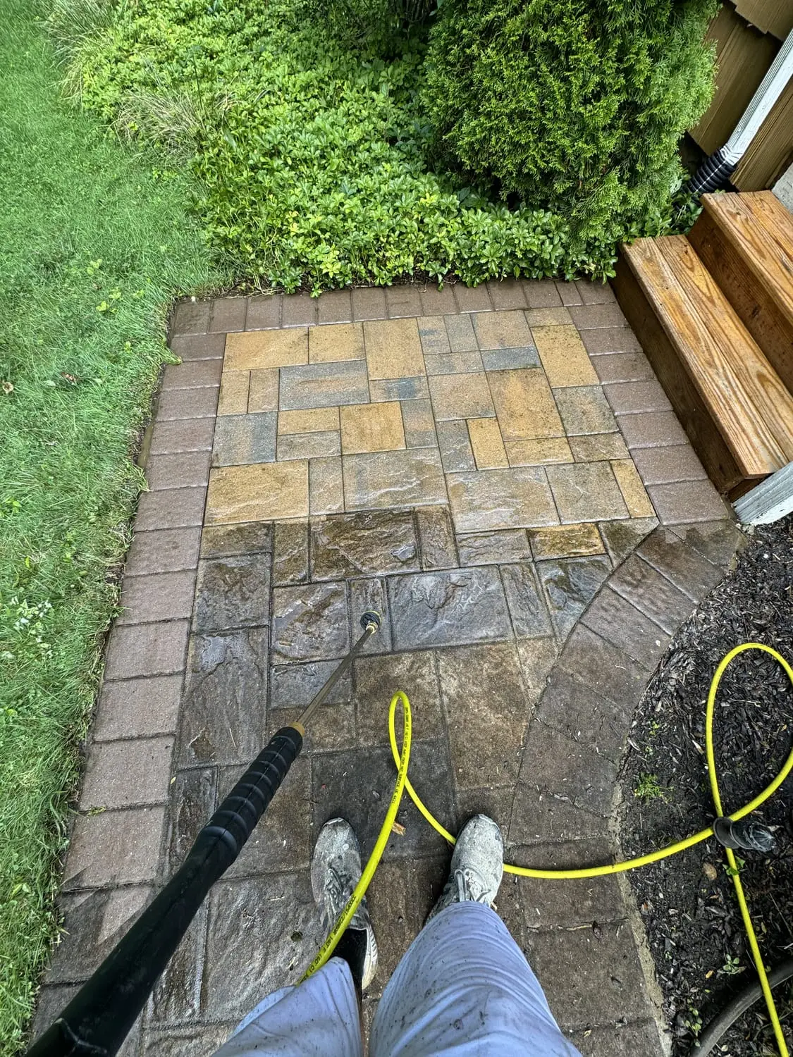 Stone paver patio caught mid power wash, the cleaned half bright against the grimy half
