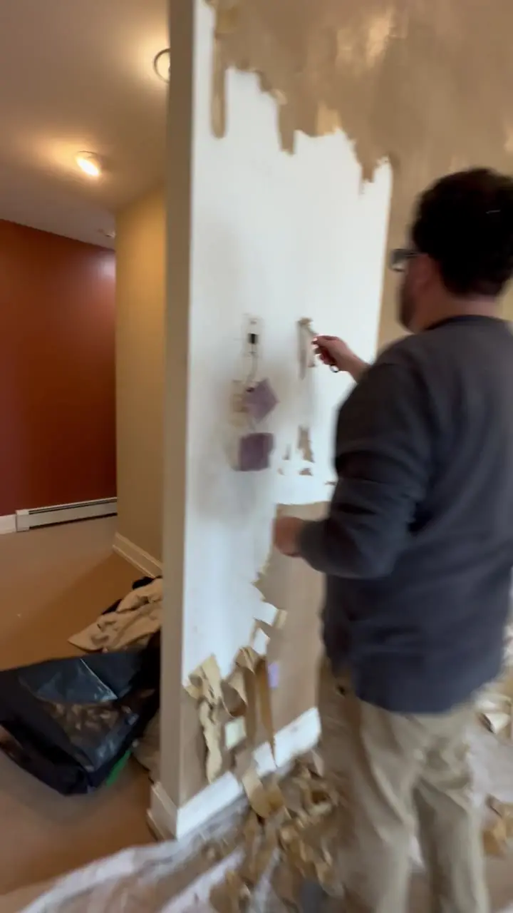 Painter stripping wallpaper from a hallway wall with drop cloths covering the floor